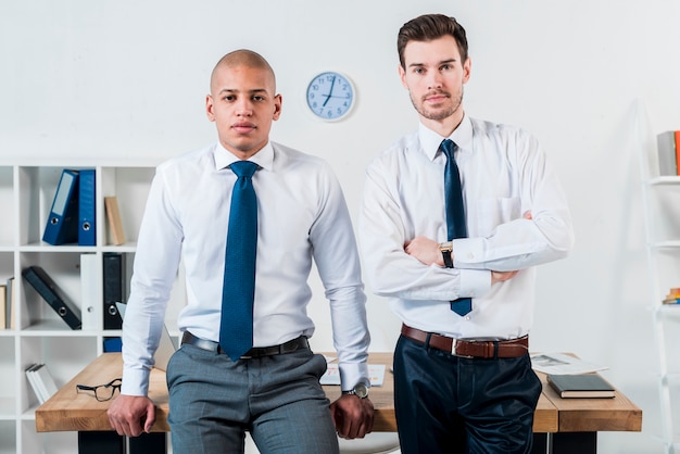 Free photo portrait of two confident young businessman standing in front of desk at office