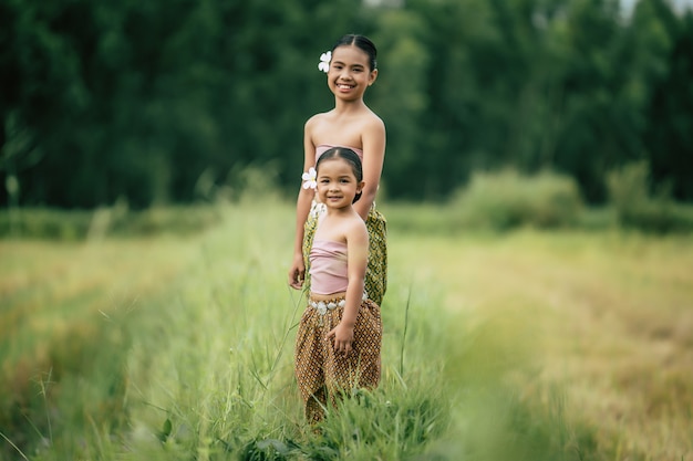 Portrait of two Cute girls in Thai traditional dress walking on rice field, They are smile with happiness, copy space