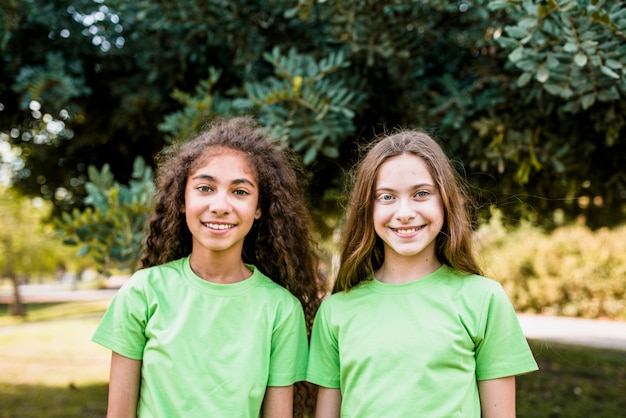 Portrait of two cute girls wearing green t-shirt standing in park