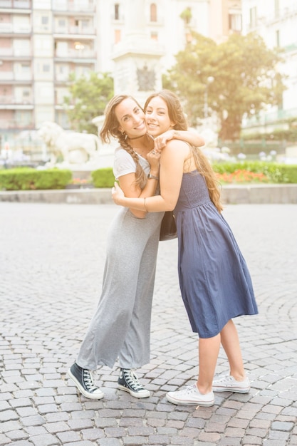 Portrait of two female friends embracing each other standing on pavement