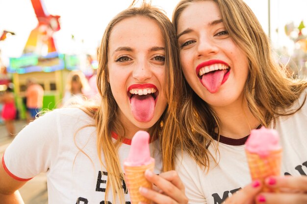 Portrait of two female friends with ice cream sticking out tongue