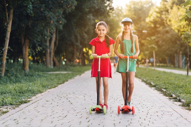 Portrait of two girls standing on push scooter in the park