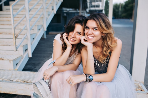 Portrait of two pretty girls in tulle skirts sitting outdoor on stairs. They smiling .