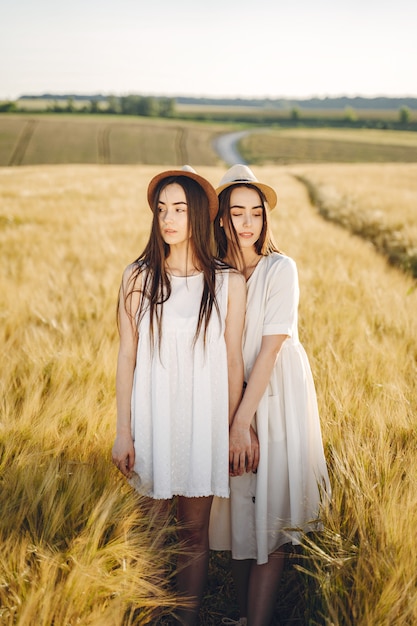 Portrait of two sisters in white dresses with long hair in a field