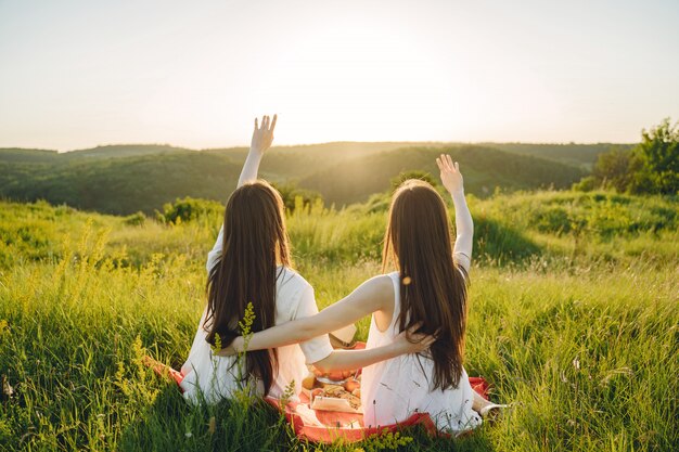 Portrait of two sisters in white dresses with long hair in a field