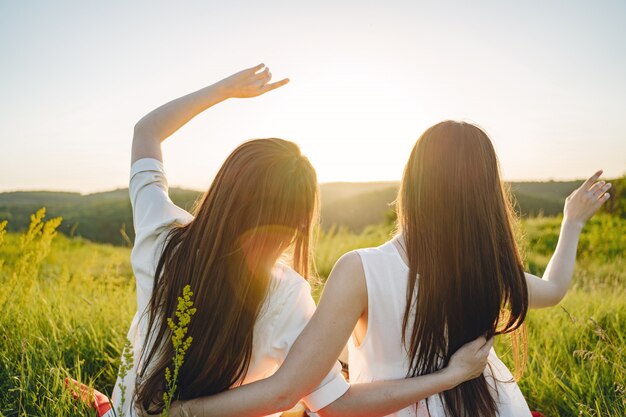 portrait of two sisters in white dresses with long hair in a field