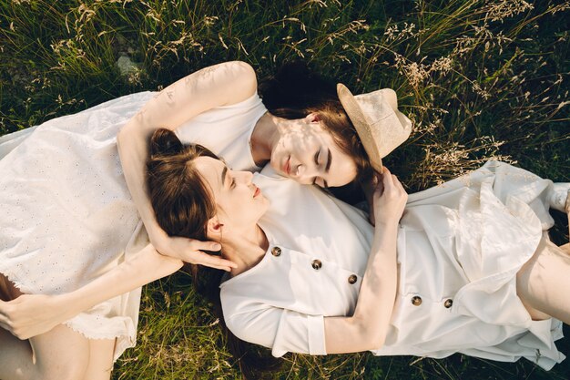 Portrait of two sisters in white dresses with long hair in a field