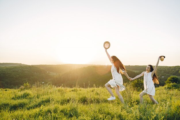 Portrait of two sisters in white dresses with long hair in a field