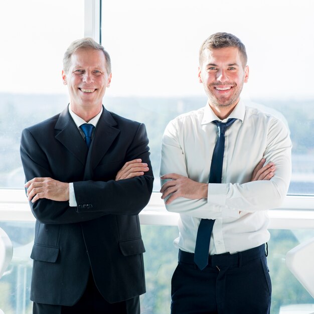 Портрет двух улыбающихся бизнесменов, стоящих около окна