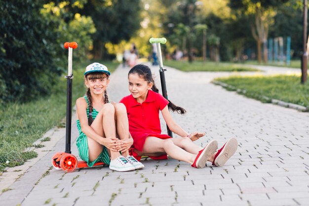 Portrait of two smiling female friends sitting on push scooter