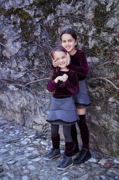 Portrait of two sweet girlfriends posing outdoor on grey natural rock background.