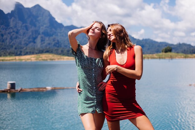 Portrait of two woman tourist friends in summer dresses on vacation travel around Thailand Khao Sok lake with beautiful mountain view.