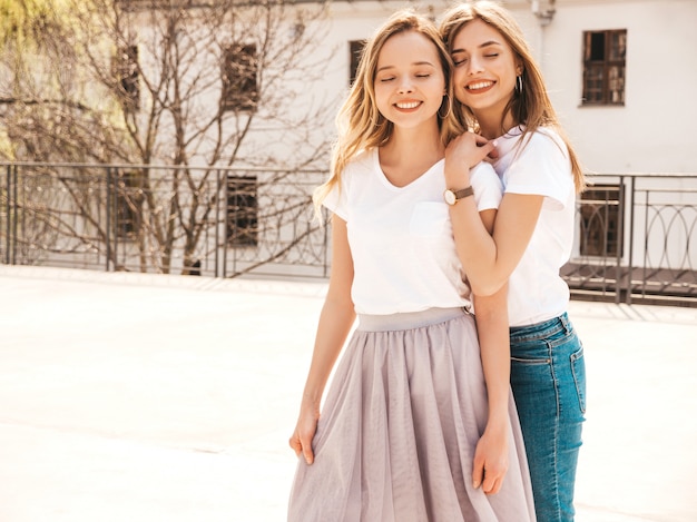 Portrait of two young beautiful blond smiling hipster girls in trendy summer white t-shirt clothes.   . Positive models having fun.Hugging