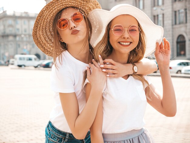 Portrait of two young beautiful blond smiling hipster girls in trendy summer white t-shirt clothes.  