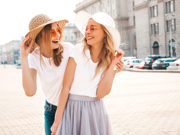 Portrait of two young beautiful blond smiling hipster girls in trendy summer white t-shirt clothes.  