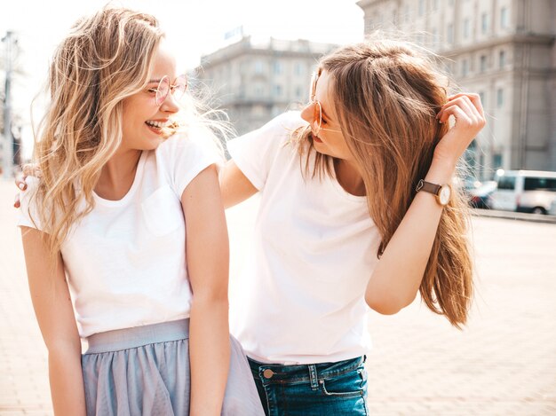 Portrait of two young beautiful blond smiling hipster girls in trendy summer white t-shirt clothes.  