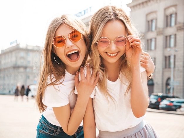 トレンディな夏の白いtシャツ服で流行に敏感な女の子を笑顔2つの若い美しいブロンドの肖像画。