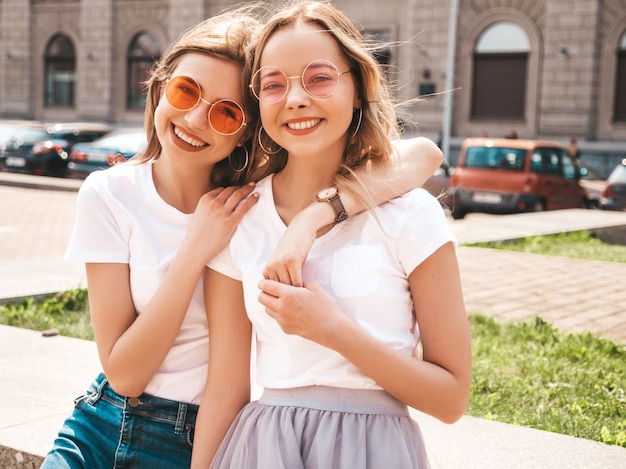 Foto gratuita un ritratto di due giovani belle ragazze sorridenti bionde dei pantaloni a vita bassa in vestiti bianchi della maglietta dell'estate d'avanguardia.