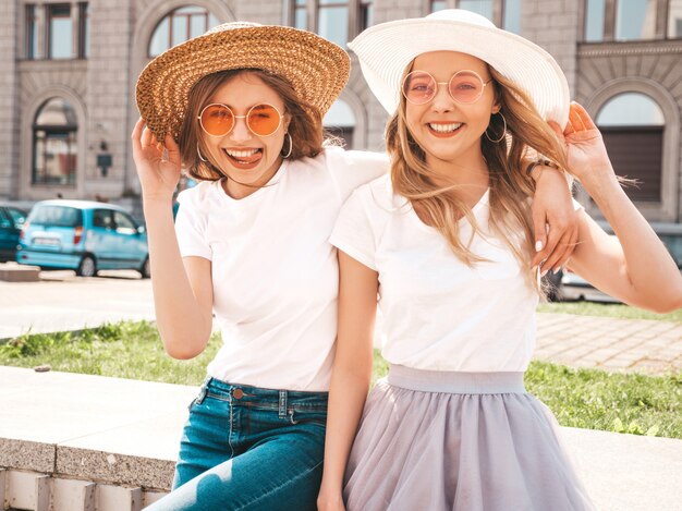 Portrait of two young beautiful blond smiling hipster girls in trendy summer white t-shirt clothes.  