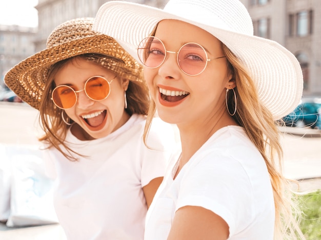 Portrait of two young beautiful blond smiling hipster girls in trendy summer white t-shirt clothes.  