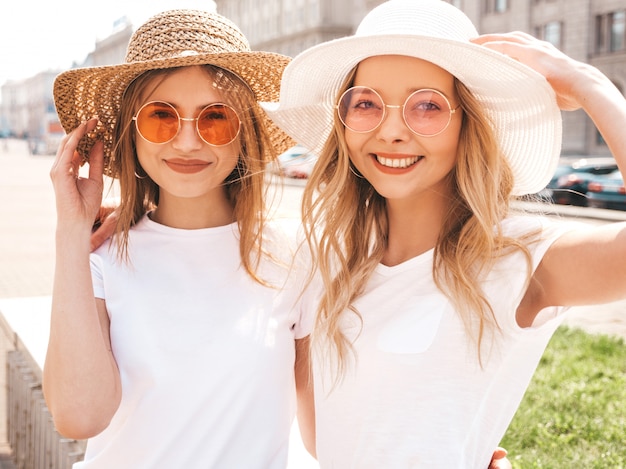 Portrait of two young beautiful blond smiling hipster girls in trendy summer white t-shirt clothes. 