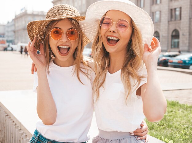 Portrait of two young beautiful blond smiling hipster girls in trendy summer white t-shirt clothes.  