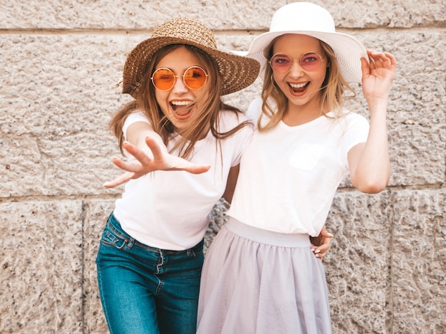 Foto gratuita un ritratto di due giovani belle ragazze sorridenti bionde dei pantaloni a vita bassa in vestiti bianchi della maglietta dell'estate d'avanguardia.