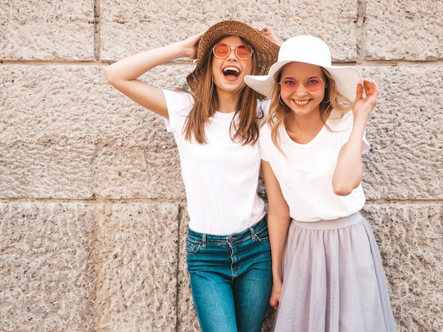 Портрет двух молодых красивых белокурых улыбающихся хипстерских девочек в модной летней белой футболке одевается.