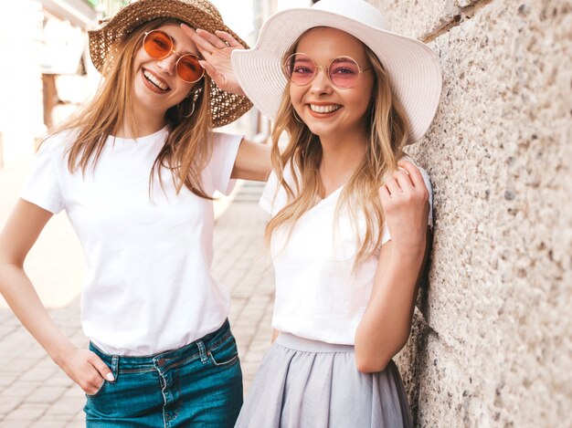 Portrait of two young beautiful blond smiling hipster girls in trendy summer white t-shirt clothes.  . 