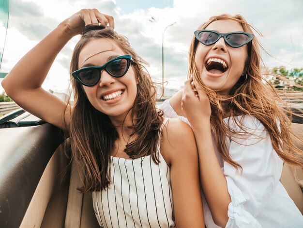 Портрет двух молодых красивых и улыбающихся хипстерских женщин в кабриолете