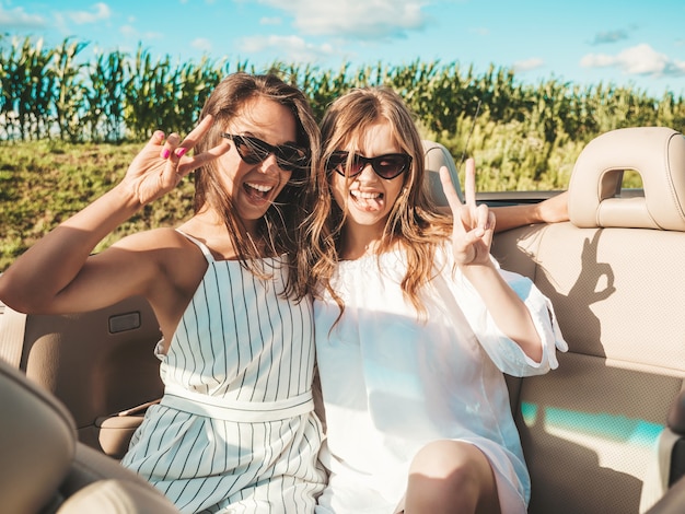 Portrait of two young beautiful and smiling hipster female in convertible car