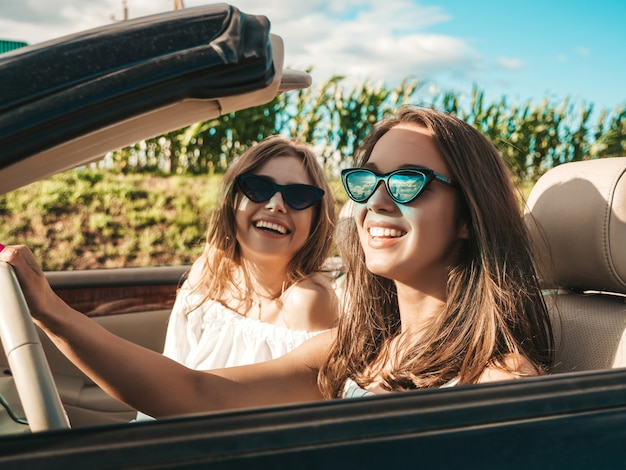 Портрет двух молодых красивых и улыбающихся хипстерских женщин в кабриолете