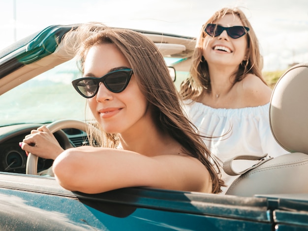 Portrait of two young beautiful and smiling hipster female in convertible car