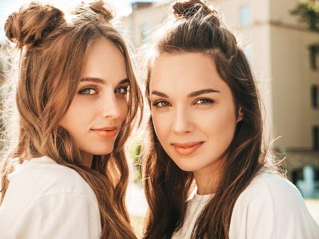 Portrait of two young beautiful smiling hipster female in trendy summer white t-shirt clothes