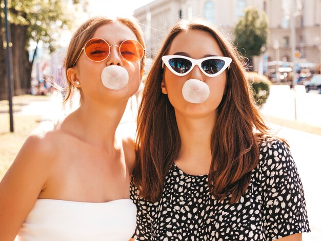 Portrait of two young beautiful smiling hipster girls in trendy summer clothes