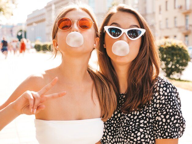 Portrait of two young beautiful smiling hipster girls in trendy summer clothes.