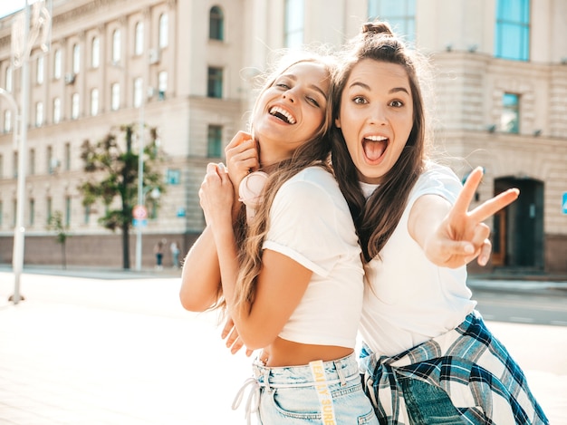 Портрет двух молодых красивых улыбающихся хипстерских девушек в модной летней белой футболке