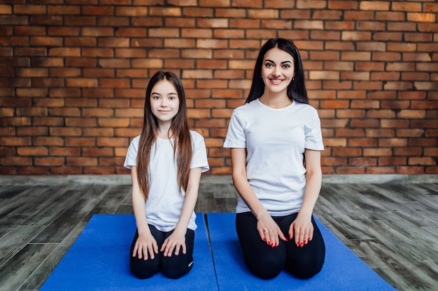 Portrait of  two young flexible girls  sitting on yoga mat and preparing before training..