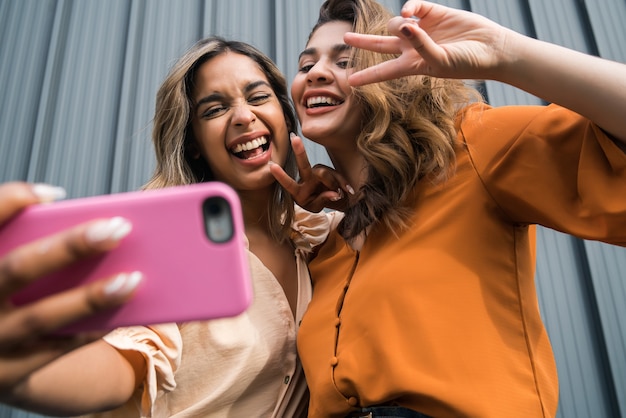 Portrait of two young friends having fun together and taking a selfie with a mobile phone outdoors