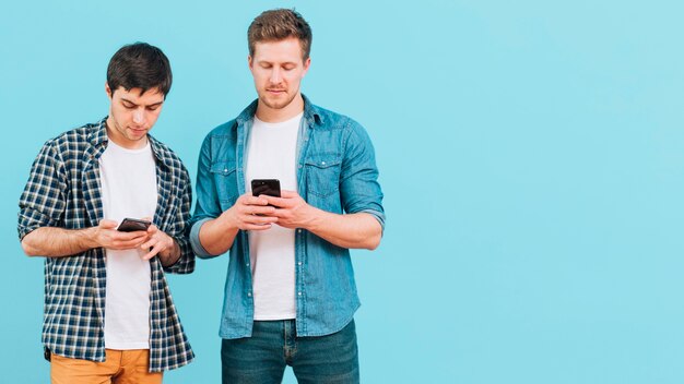 Portrait of two young men standing against blue background using mobile phone