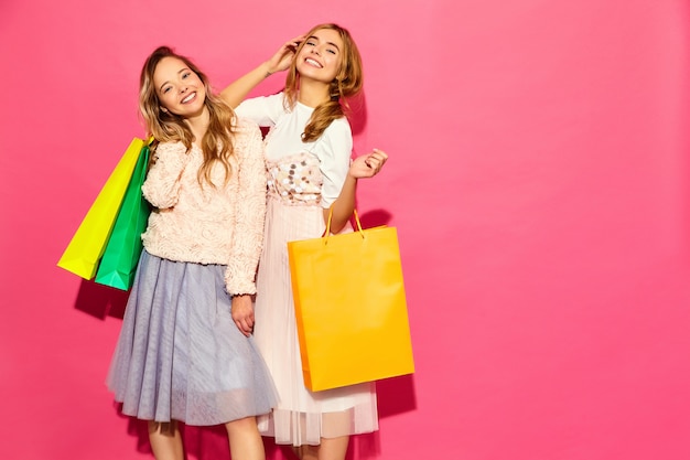 쇼핑백을 들고 두 젊은 세련 된 웃는 금발 여자의 초상화. 여자 여름 hipster 옷을 입고. 분홍색 벽 위에 포즈를 취하는 긍정적 인 모델