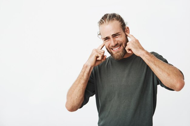 Portrait of unhappy bearded man closing ears with fingers with annoyed expression