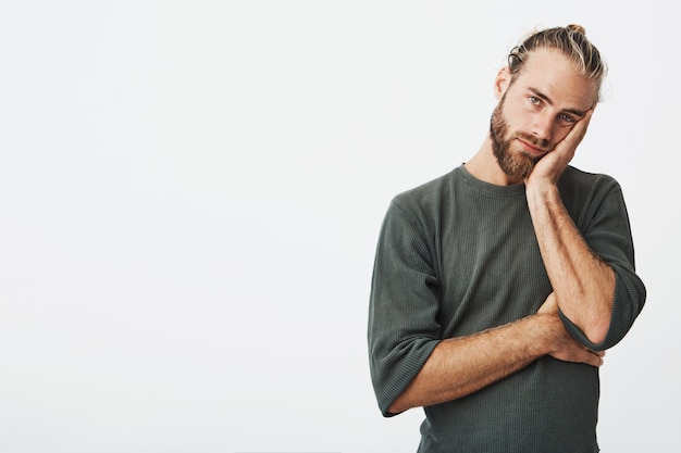 Portrait of unhappy mature bearded guy in grey shirt holding hand on cheek exhausted and tired