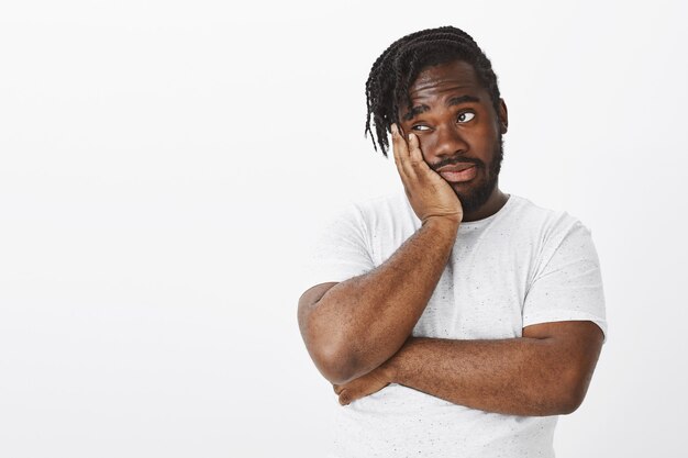 Portrait of unimpressed guy with braids posing against the white wall