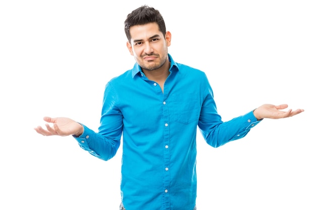 Портрет неуверенного мужчины в синей рубашке, пожимающего плечами на белом фоне