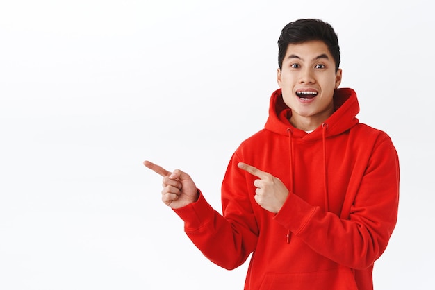 Free photo portrait of upbeat enthusiastic young man describing awesome event coming soon pointing fingers left inviting to come together look impressed and happy tell fantastic news white background