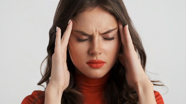 Portrait of upset brunette girl showing headache on camera over white background