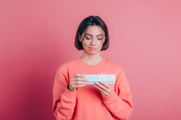 Portrait of upset frustrated girl opening gift box isolated on pink background