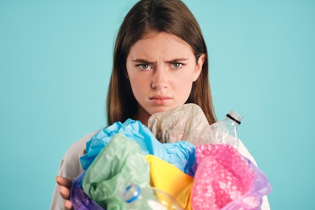 Portrait of upset girl holding plastic waste sadly looking in camera over colorful background isolated