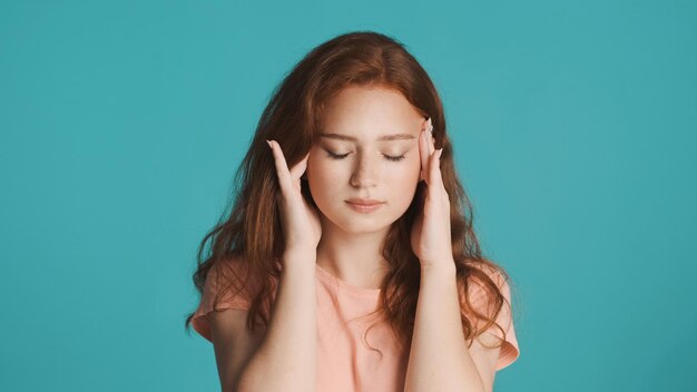 Портрет расстроенной рыжей девушки, показывающей головную боль на камеру на красочном фоне Усталое выражение лица